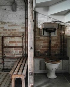 an old bathroom with exposed brick walls and a toilet in the corner next to a wooden slatted bench