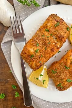 two pieces of fried fish on a plate with lemon wedges and parmesan cheese