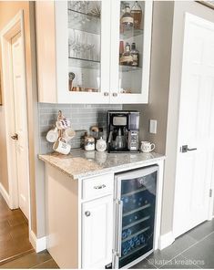 a wine cooler in the corner of a kitchen with white cabinets and marble counter tops