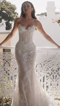 a woman in a wedding dress standing on a balcony with her arms out and hands behind her back