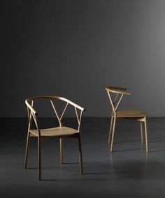 two wooden chairs sitting next to each other on a dark floor in front of a wall