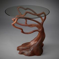 a wooden table with glass top and tree design on the bottom, in front of a gray background