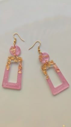 the pink and gold earrings are hanging from hooks on white tablecloth with small beads