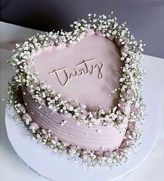 there is a pink cake with white flowers on the top and writing that says happy