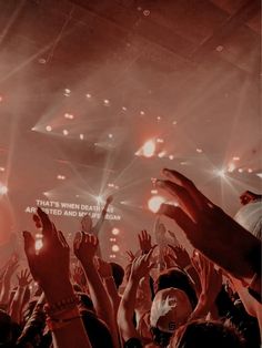 a crowd of people at a concert with their hands in the air and lights on