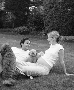 a man and woman sitting on the grass with a dog