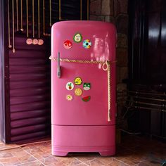 a pink refrigerator with stickers on it sitting in front of a brick wall and door