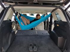 a woman sitting in a blue hammock on the back of a car trunk