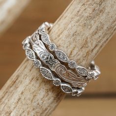 a stack of silver rings sitting on top of a piece of wood with an intricate design