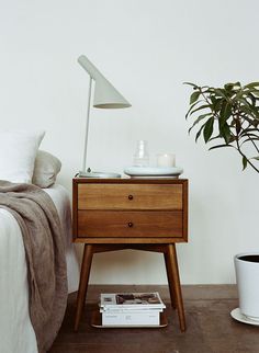 a bedroom with a bed, nightstand and potted plant on the floor next to it