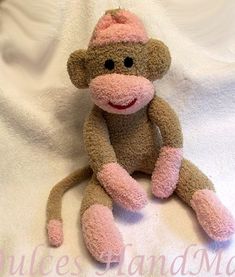 a stuffed monkey wearing a pink hat sitting on a white sheet