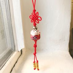 a red string hanging from a window sill in front of a white wall with a glass bead on it