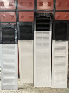 three white and black shutters in front of a wall with red accents on it