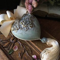 a heart shaped box with flowers and ribbons on it sitting on a table next to an open book