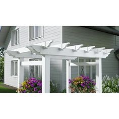 a white pergola on the side of a house with flowers in front of it