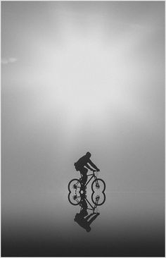 a person riding a bike on top of a body of water in front of a cloudy sky