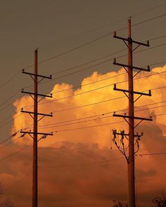 there are many telephone poles and wires in the sky with clouds behind them at sunset