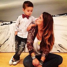 a woman sitting on the floor with a young boy in her lap and an art work behind her