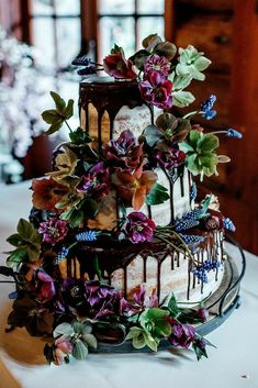 a three tiered cake with purple flowers and chocolate icing on the top layer