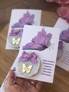 two cards with purple butterflies on them are being held by someone's left hand