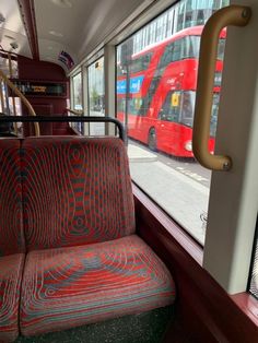 a red double decker bus traveling down a street next to a tall building with windows