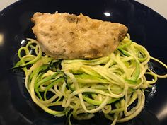 a black plate topped with zucchini noodles and chicken breast on top of it