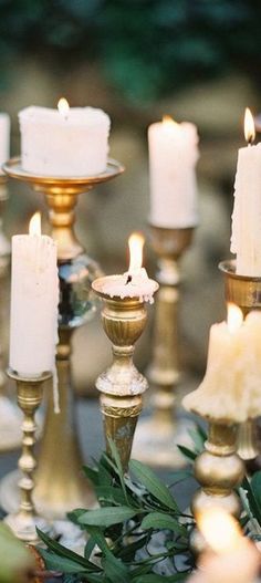 several candles are lit on a table with greenery