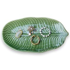 a green leaf shaped platter with rings and bracelets sitting on top of it