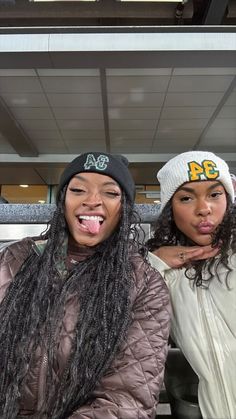 two women with long hair and beanies posing for the camera in front of a bus