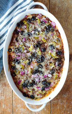 a casserole dish with olives, onions and cheese in it on a wooden table