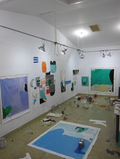 an art studio with multiple paintings on the wall and various pieces of paper taped to the floor