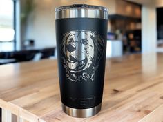 a stainless steel tumbler with a dog's face on it sitting on a wooden table