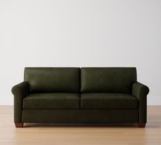 a green couch sitting on top of a hard wood floor next to a white wall