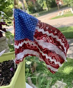 an american flag hanging from a pole in a flower pot with dirt and grass around it