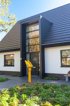 a house with a black roof and white walls has a bright yellow object in front of it