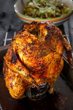 a whole chicken sitting on top of a table next to a bowl of salad and a bottle of beer