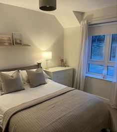 a bed sitting under a window next to a night stand with two lamps on top of it