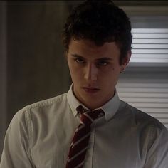 a young man wearing a white shirt and red tie looking at the camera while standing in front of a window