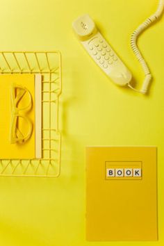 a yellow desk with a phone, book and remote control on the table next to it