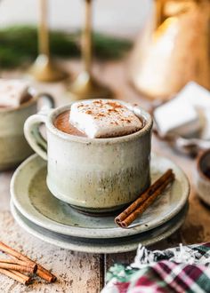 two cups filled with hot chocolate and cinnamon on top of a plate next to some cinnamon sticks