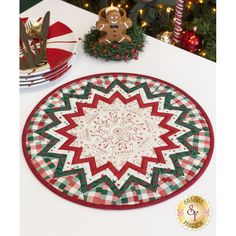 a white table topped with a red and green placemat next to a christmas tree