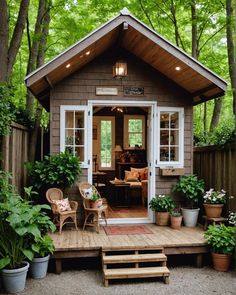 a small wooden cabin in the woods with potted plants on the porch and steps leading up to it