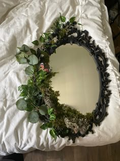 a round mirror sitting on top of a bed covered in leaves and plants next to a pair of black shoes