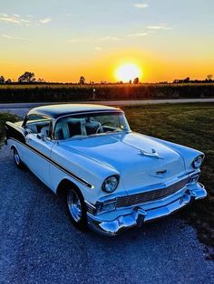 an old car is parked on the side of the road as the sun goes down