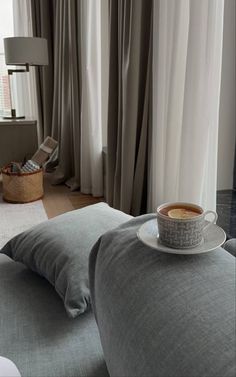 a cup of coffee sitting on top of a pillow in front of a large window