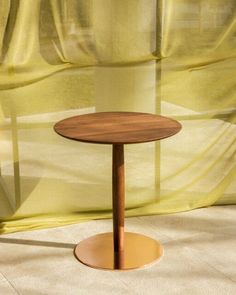 a small wooden table sitting in front of a yellow drapes covered window with curtains behind it