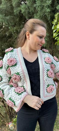 a woman wearing a crocheted jacket with pink roses on the sleeves and shoulders