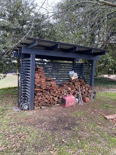 a pile of firewood sitting under a tree next to a metal structure on top of grass