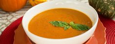 a white bowl filled with soup on top of a red place mat next to pumpkins