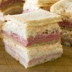 several sandwiches stacked on top of each other with meat and cheese in the middle, sitting on a cutting board